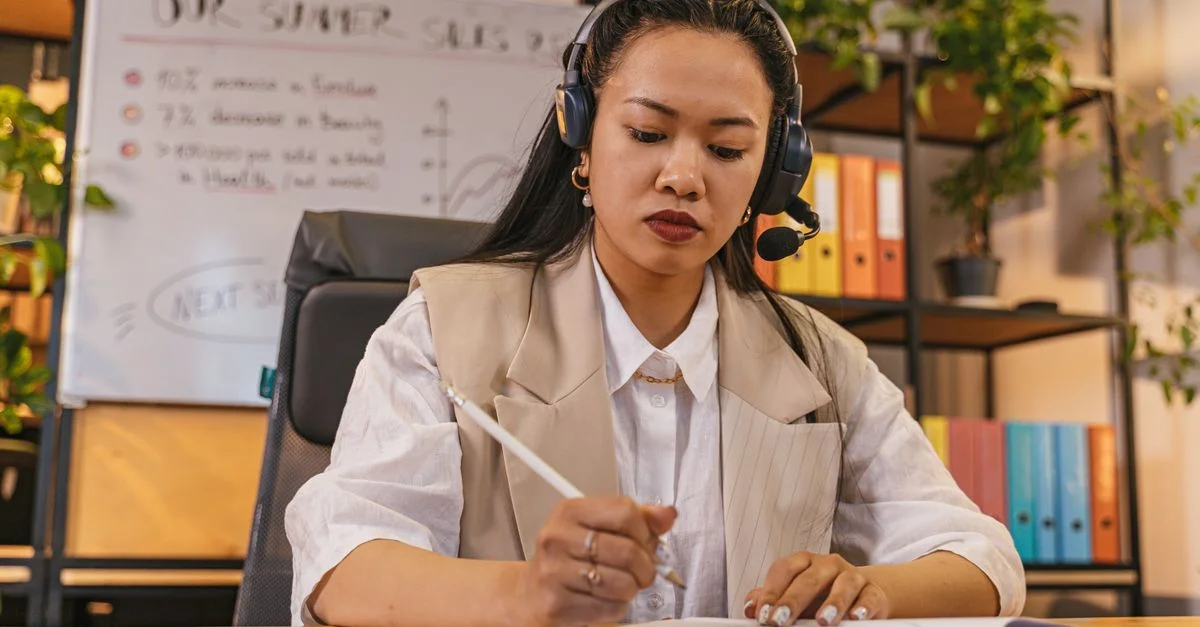 Femme professionnelle portant un casque, prenant des notes dans un cadre de bureau, concentrée sur son travail.