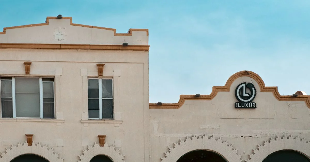 Élégant bâtiment blanc orné d'une enseigne Luxur et de fenêtres cintrées se détachant sur un ciel bleu.