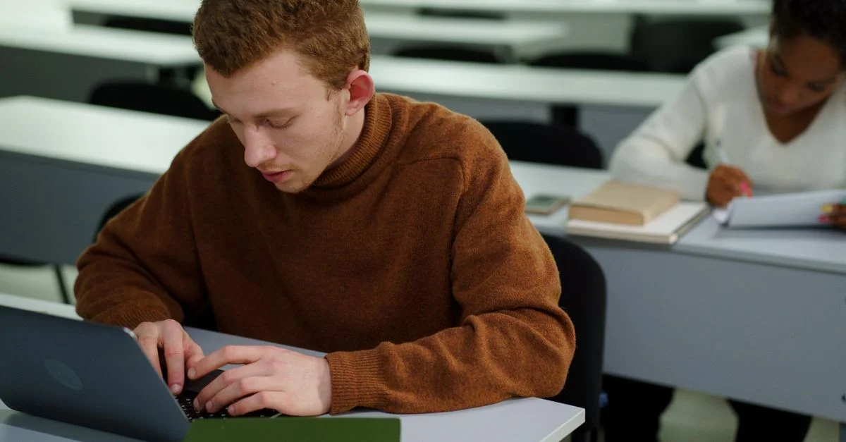 Deux étudiants se concentrant sur leur travail dans un cadre de classe, utilisant des ordinateurs portables.