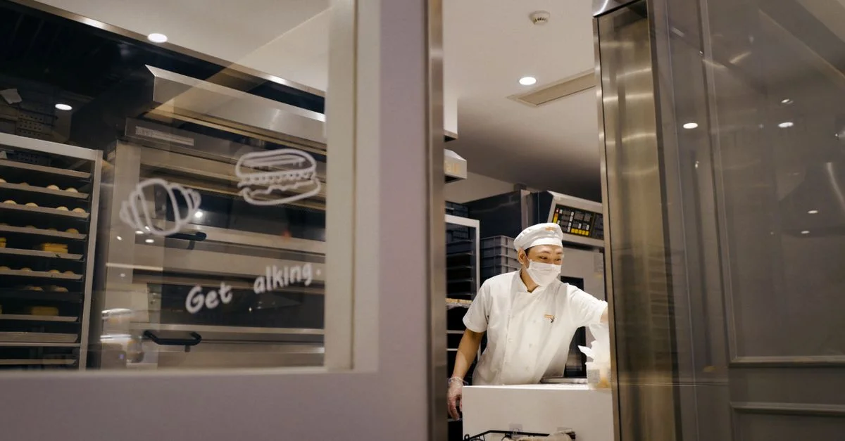 Boulanger dans une cuisine commerciale préparant des produits de boulangerie avec un équipement professionnel.