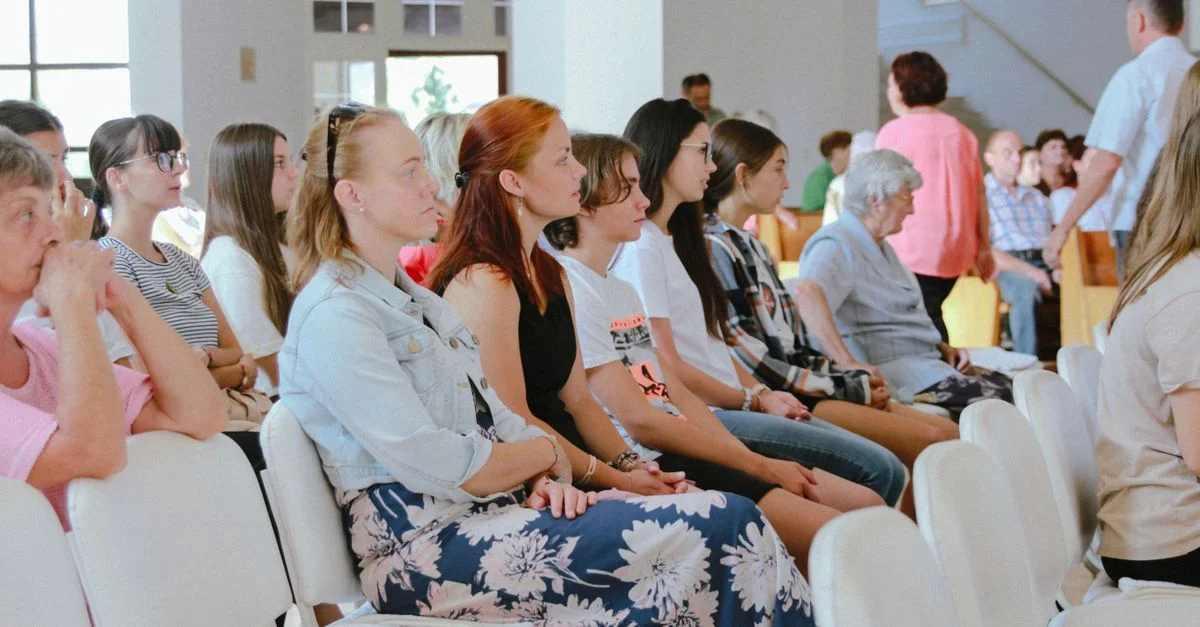 Un groupe diversifié de personnes assises attentivement lors d'une réunion ou d'un événement en intérieur, capturé dans une grande pièce.
