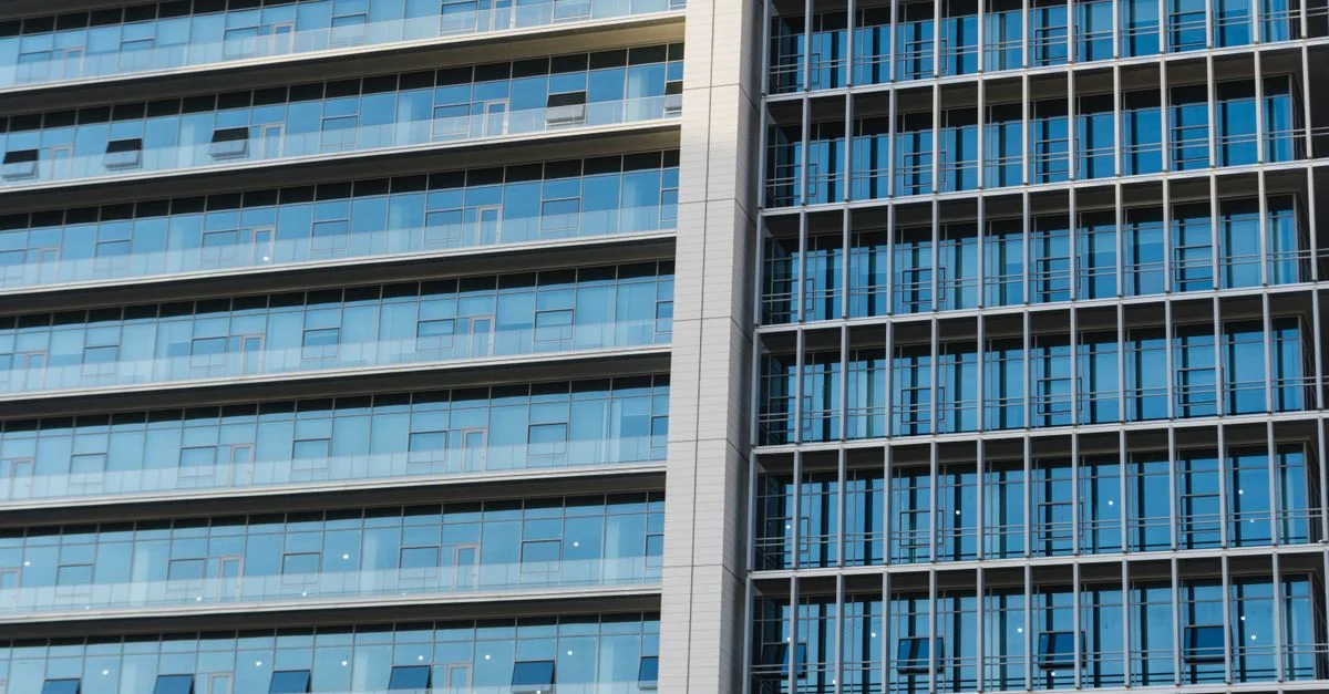 Vue détaillée d'un immeuble de bureaux moderne de grande hauteur avec des fenêtres en verre et des reflets.