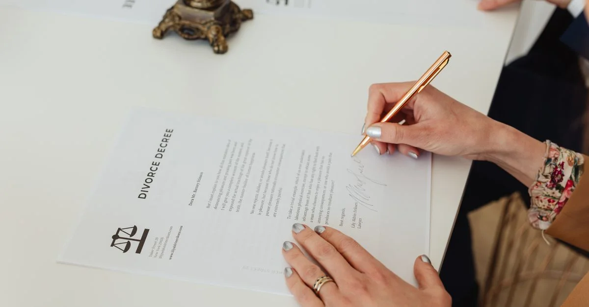 Gros plan sur des mains signant un document de divorce sur un bureau, mettant en avant le processus légal.