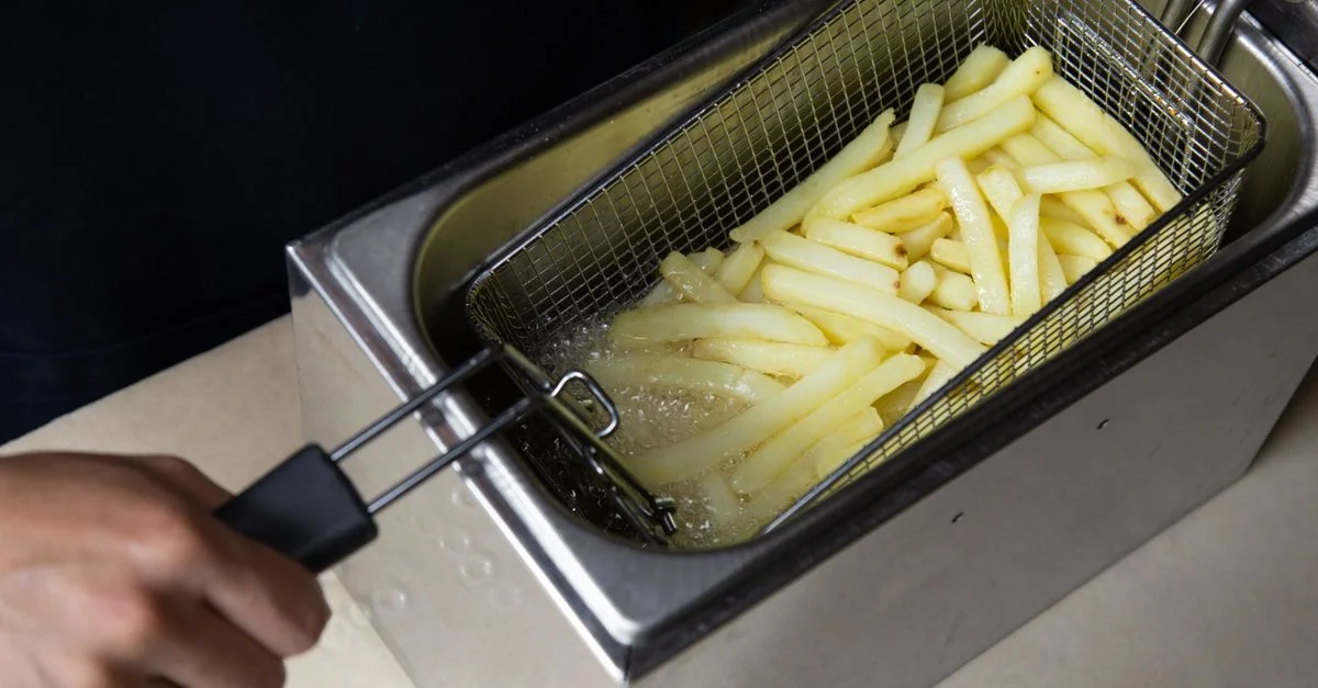 Gros plan sur des frites en train d'être frites dans une friteuse commerciale, main tenant le panier.