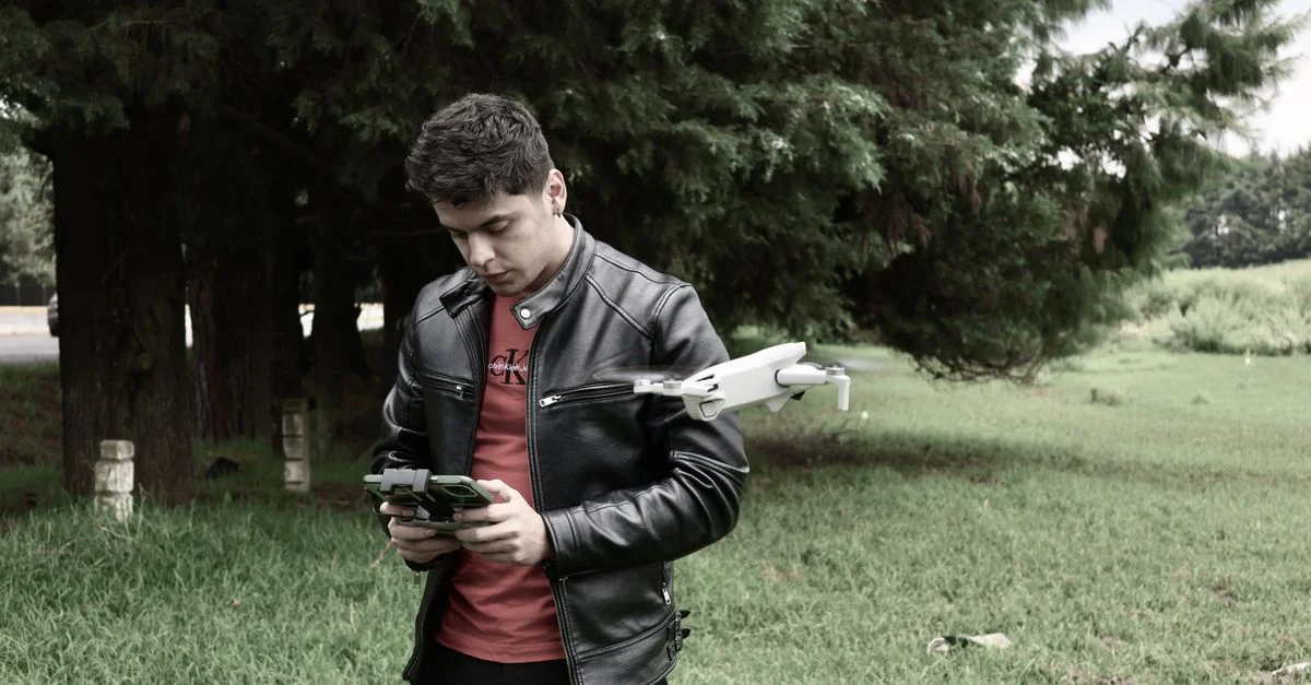 Un jeune homme avec une télécommande et un drone dans un parc verdoyant, portant une veste en cuir.