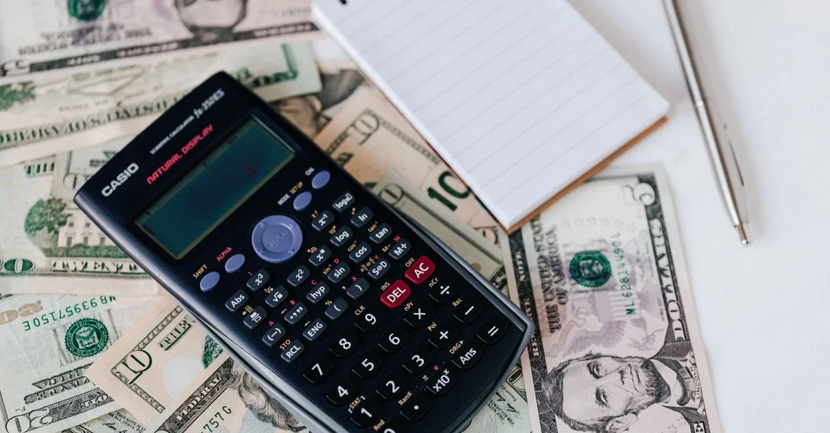Calculatrice, espèces et carnet sur la table pour planification financière.