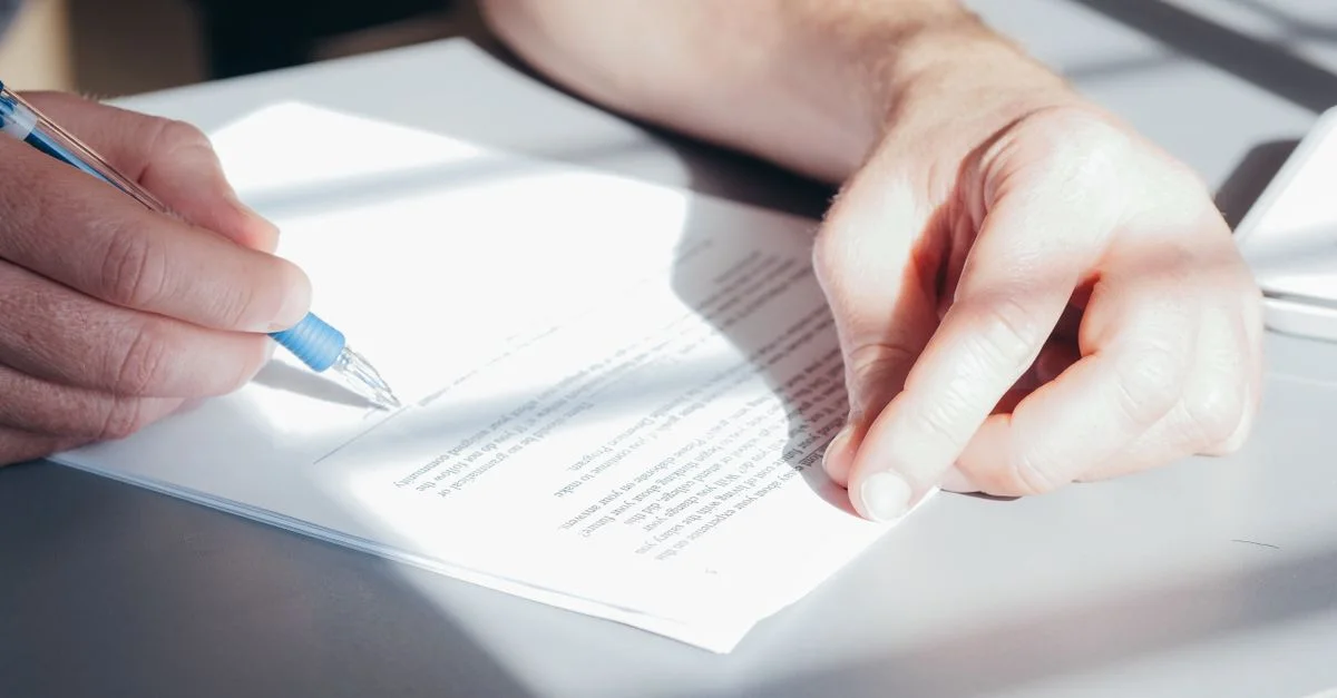 Mains signant un contrat avec un stylo bleu, vue de près.