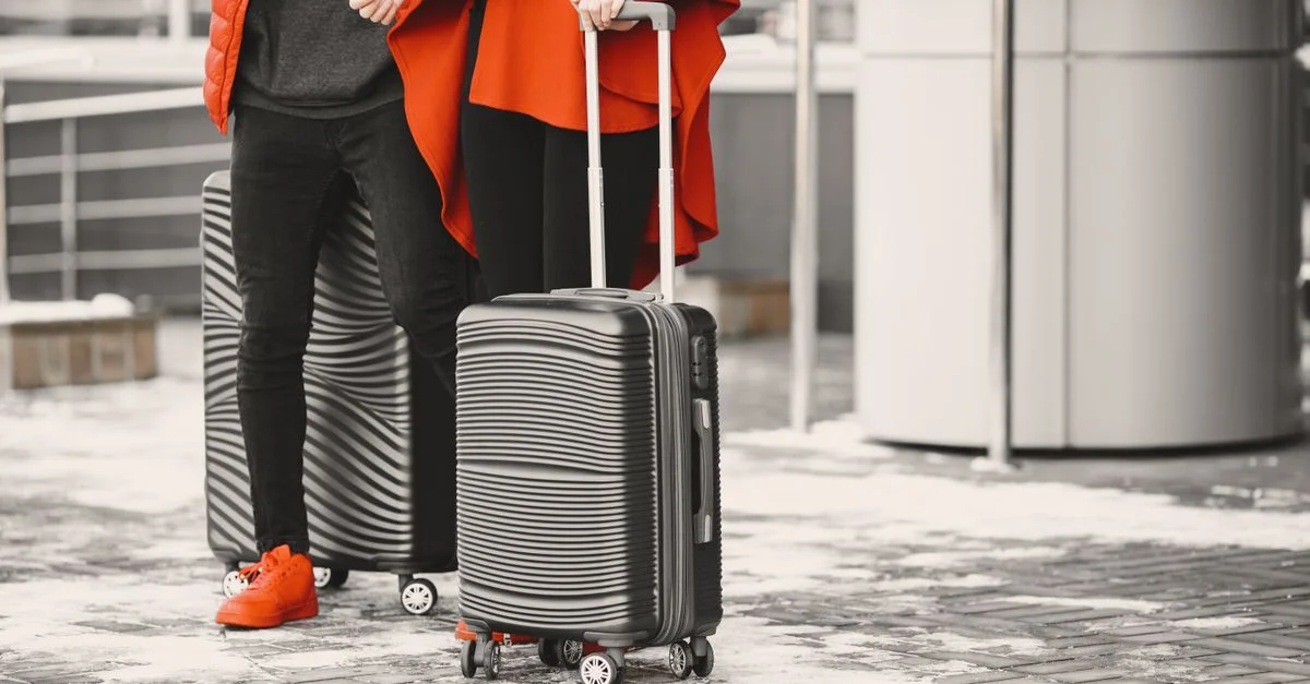 Un couple à la mode en vêtements d'hiver avec des bagages élégants, se tenant à l'extérieur par une journée neigeuse.