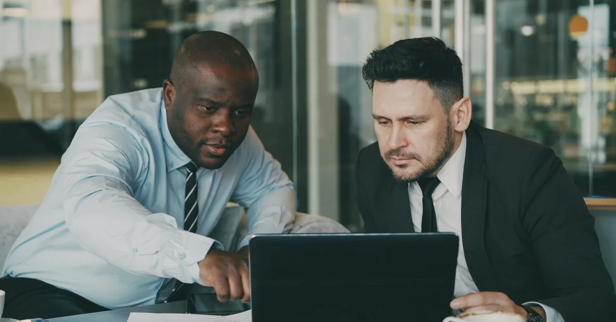 Deux hommes d'affaires se concentrant sur une tablette, collaborant dans un bureau moderne.
