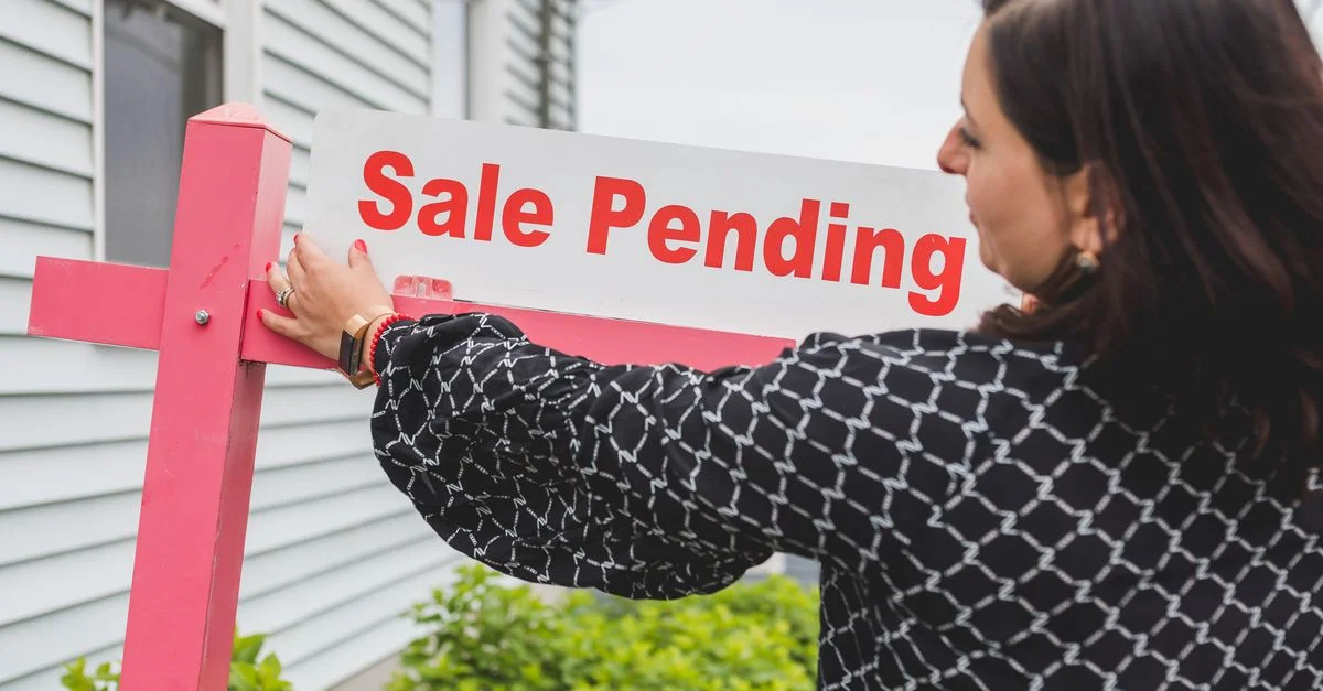 Une agente immobilière ajuste un panneau de vente en attente sur une propriété, indiquant une clôture de vente prochaine.