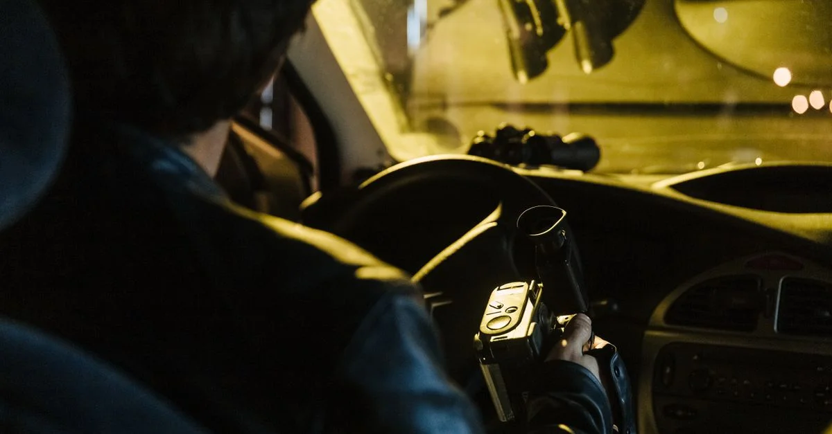 Vue de dos d'un homme enregistrant avec un caméscope à l'intérieur d'une voiture la nuit. Concept de surveillance urbaine.