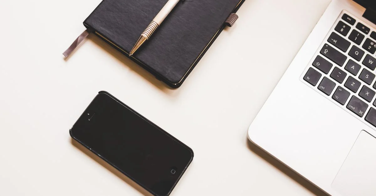 Un espace de travail épuré avec un ordinateur portable, un smartphone et un carnet sur un bureau.