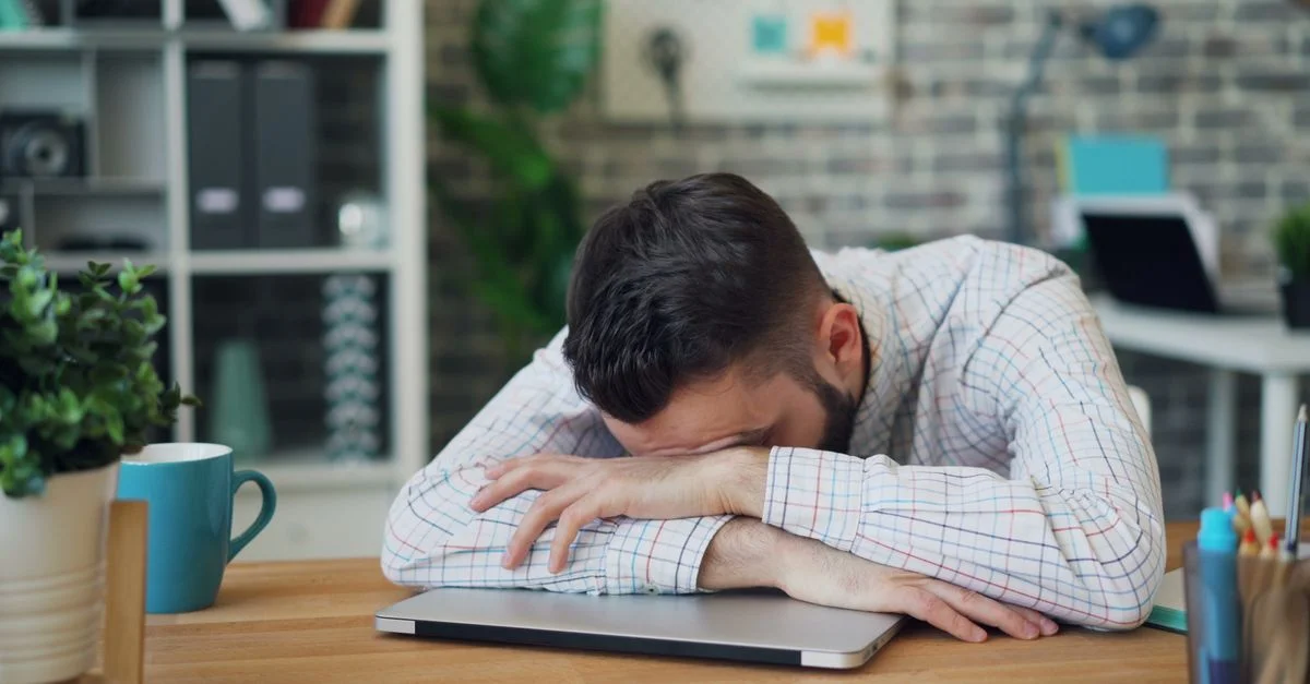 Employé de bureau fatigué reposant sa tête sur un ordinateur portable au bureau dans un bureau moderne.