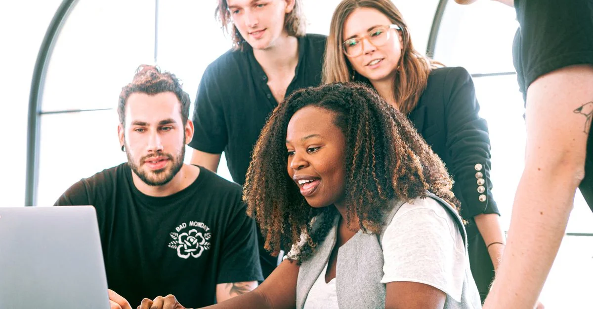 Un groupe diversifié de jeunes professionnels collaborant autour d'un ordinateur portable dans un bureau moderne. Parfait pour des concepts liés au business ou à la technologie.