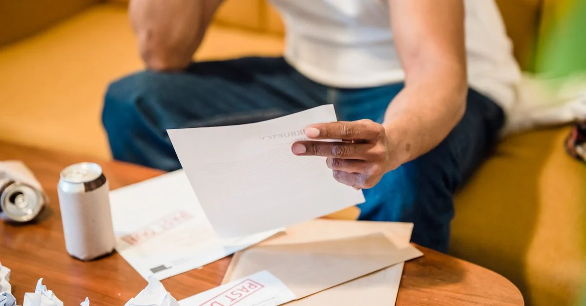 Homme assis sur un canapé, lisant des factures impayées, l'air stressé et inquiet à propos de ses dettes financières.