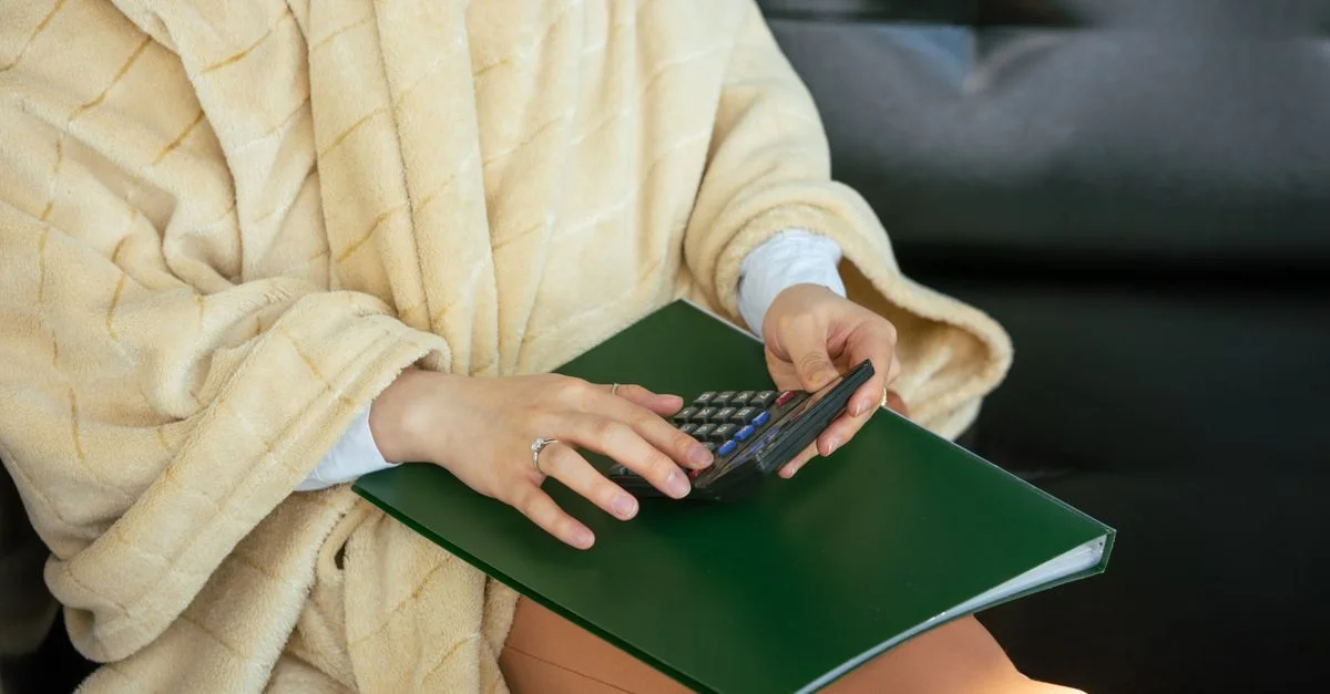 Gros plan de mains utilisant une calculatrice sur un dossier, portant un peignoir confortable.