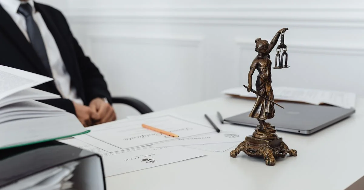 Espace de travail d'un professionnel du droit avec une statue de la Justice, des documents et un ordinateur portable.