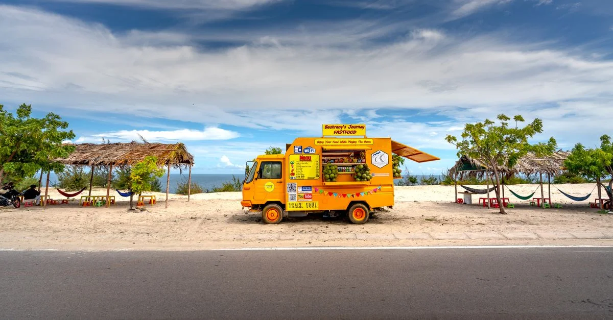 Un camion de nourriture coloré garé près de la plage propose des en-cas sous un ciel tropical.