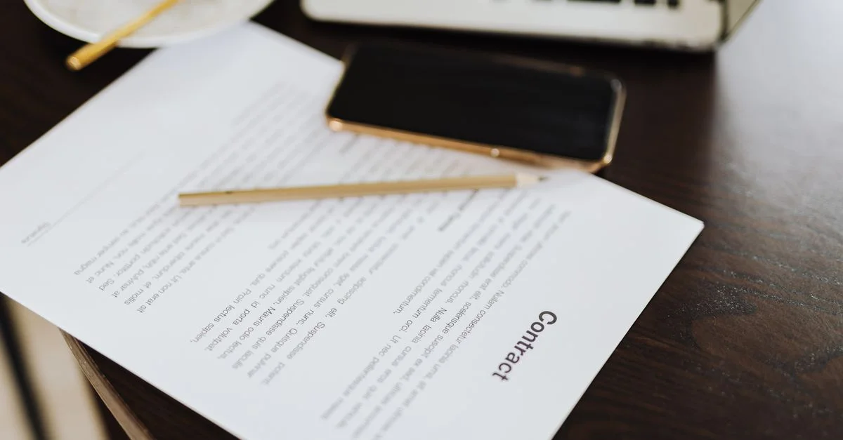 Gros plan sur un contrat avec des essentiels de bureau comme un ordinateur portable et un café sur un bureau.