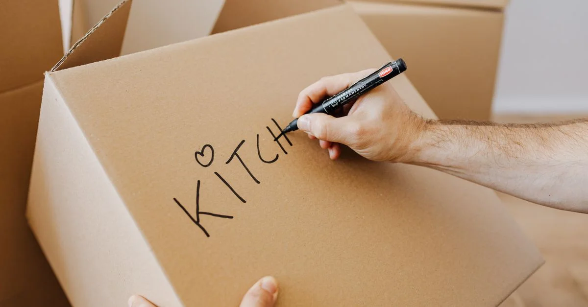 Gros plan d'une main étiquetant une boîte en carton de déménagement pour la cuisine.