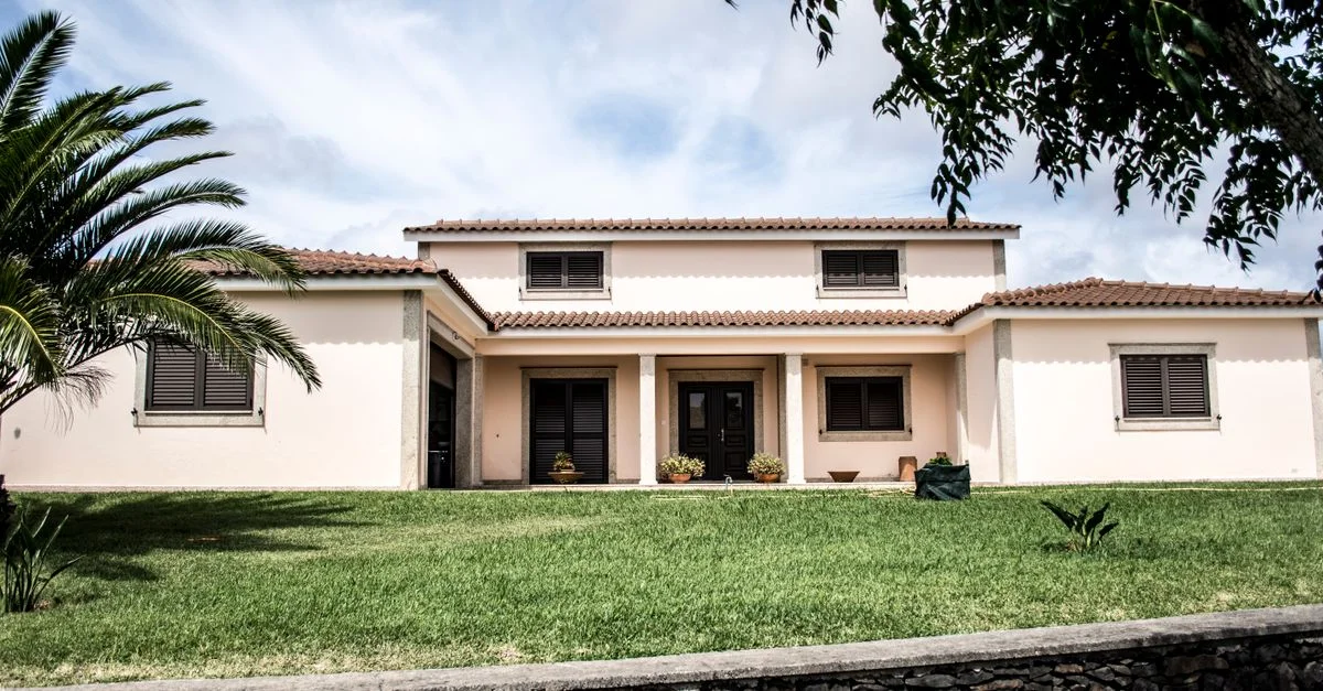 Une maison familiale moderne et élégante avec une pelouse luxuriante et un palmier sous un ciel lumineux.