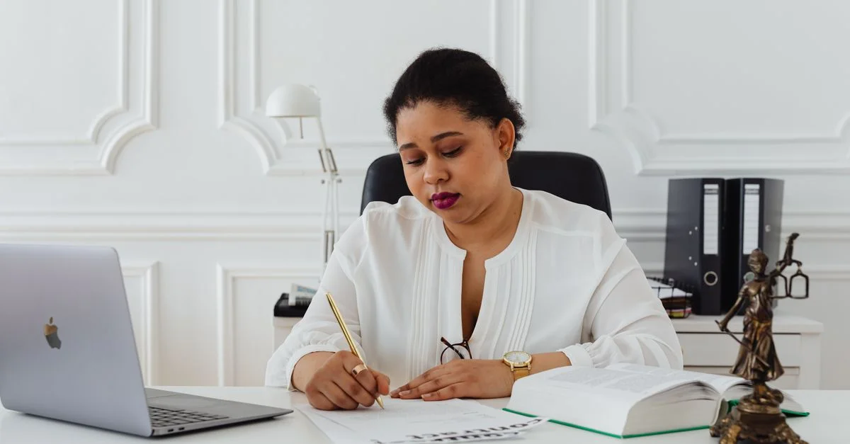 Femme avocate afro-américaine signant des documents à un bureau, symbolisant le professionnalisme.