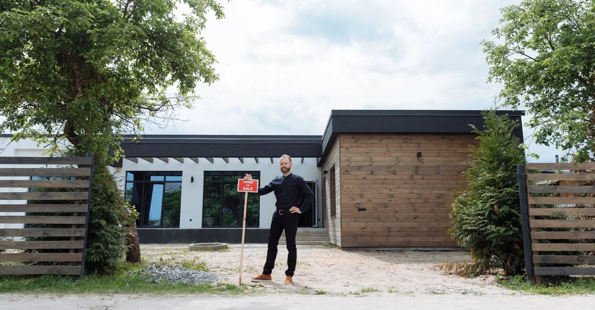Agent immobilier se tenant dehors d'une maison moderne avec un panneau à vendre, affichant un design contemporain.