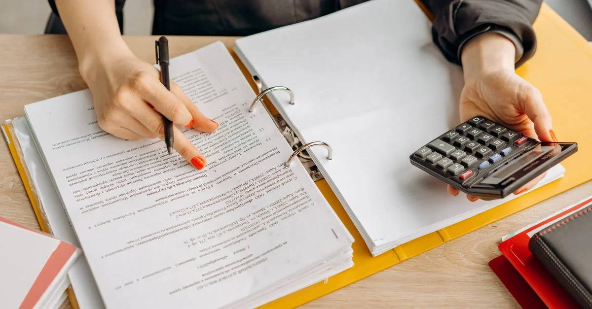 Une femme examinant des documents et utilisant une calculatrice sur une table en bois.