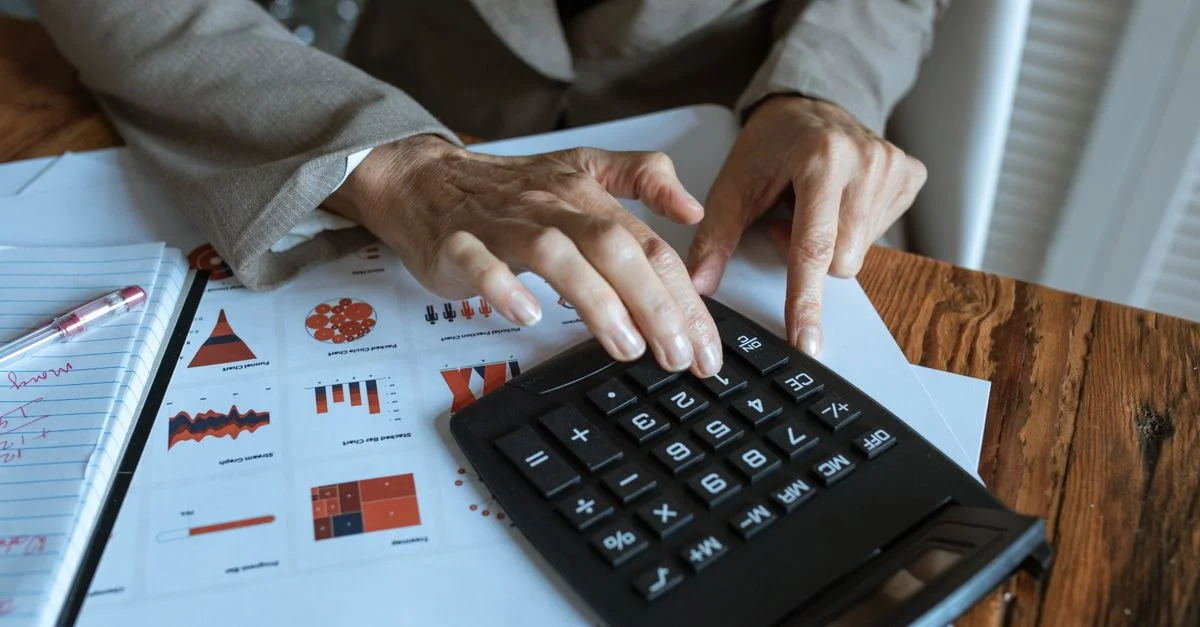 Un homme d'affaires utilisant une calculatrice pour analyser des graphiques et des tableaux financiers sur un bureau.