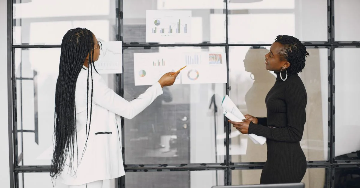 Deux femmes d'affaires discutant de graphiques financiers dans un cadre de bureau moderne.