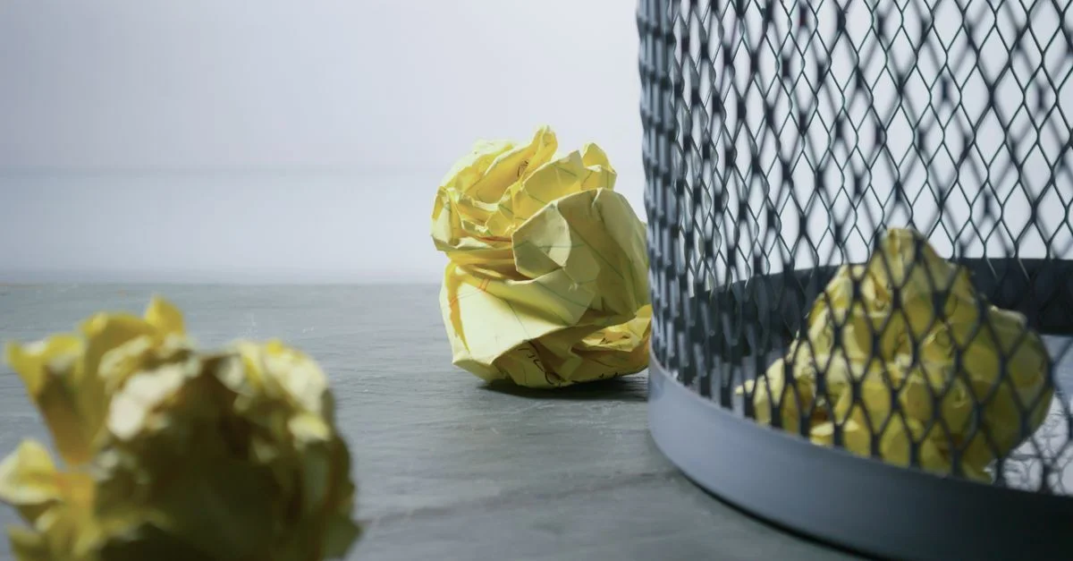 Gros plan de papier jaune froissé autour d'une poubelle en mailles, symbolisant des idées rejetées ou le recyclage.