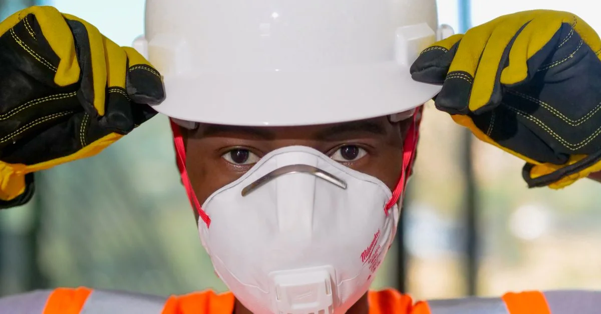 Gros plan d'un ouvrier du bâtiment portant des équipements de sécurité, y compris un casque, un masque N95 et des gants.