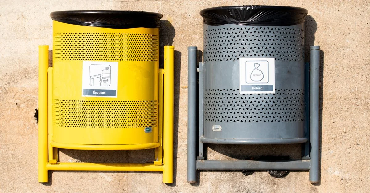Poubelles de recyclage jaunes et grises brillantes contre un mur en béton à la lumière du jour.
