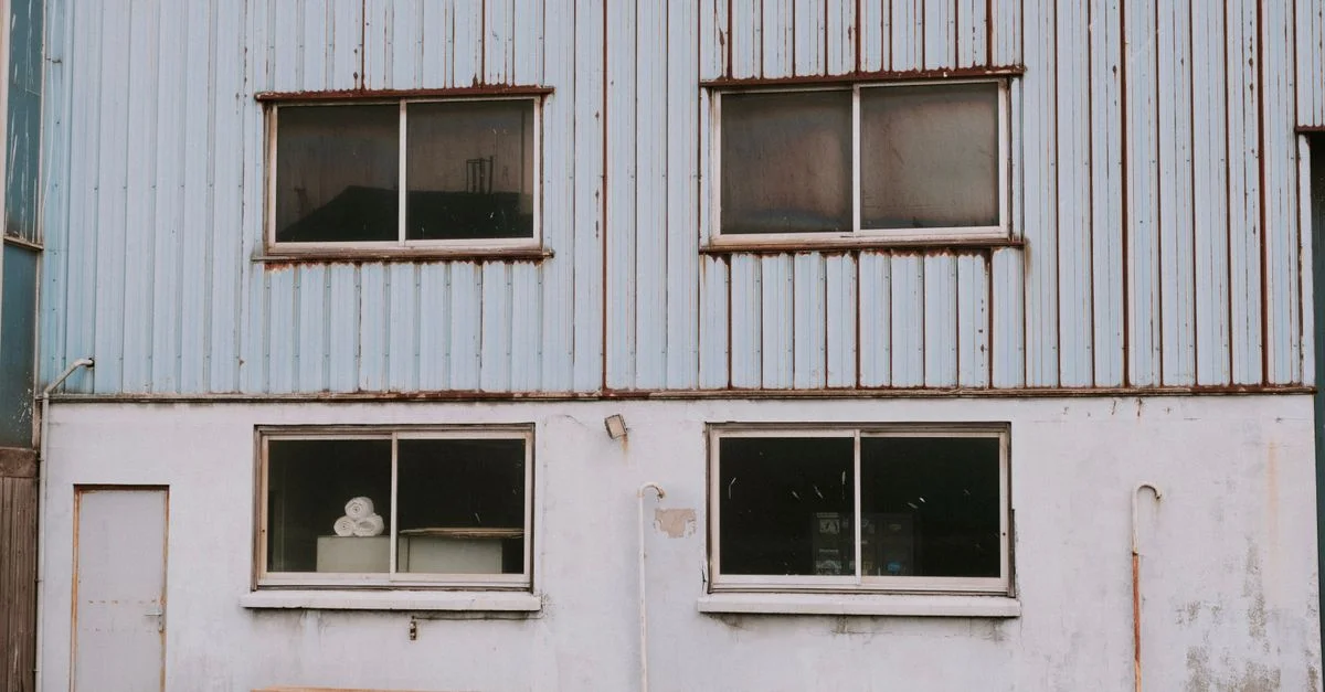 Extérieur d'un ancien bâtiment industriel avec des fenêtres montrant la décadence urbaine et un charme rustique.