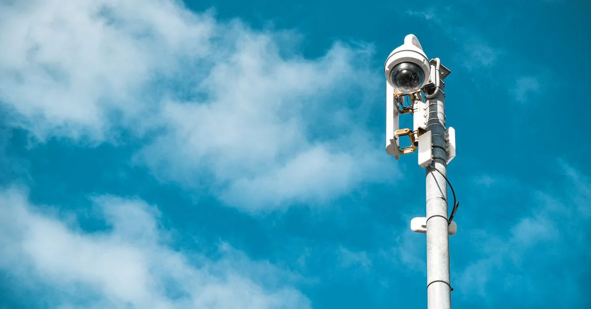 Gros plan d'une caméra de surveillance sur un poteau sous un ciel bleu clair.