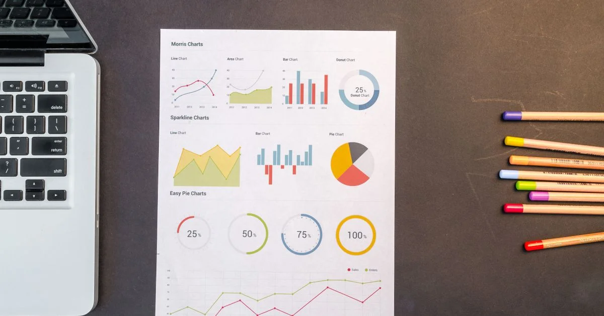 Vue plongeante de graphiques et de crayons de couleur sur un bureau à côté d'un ordinateur portable, parfait pour des thèmes commerciaux ou éducatifs.