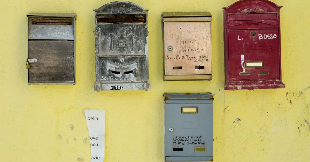 Cinq anciennes boîtes aux lettres fixées sur un mur jaune distressé, mettant en valeur le charme vintage.