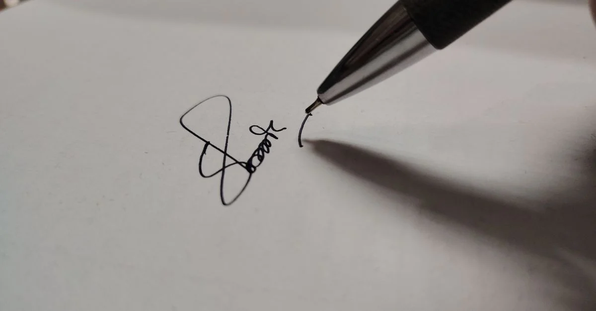 Photo macro d'un stylo écrivant une signature sur du papier blanc, mettant en avant la précision.