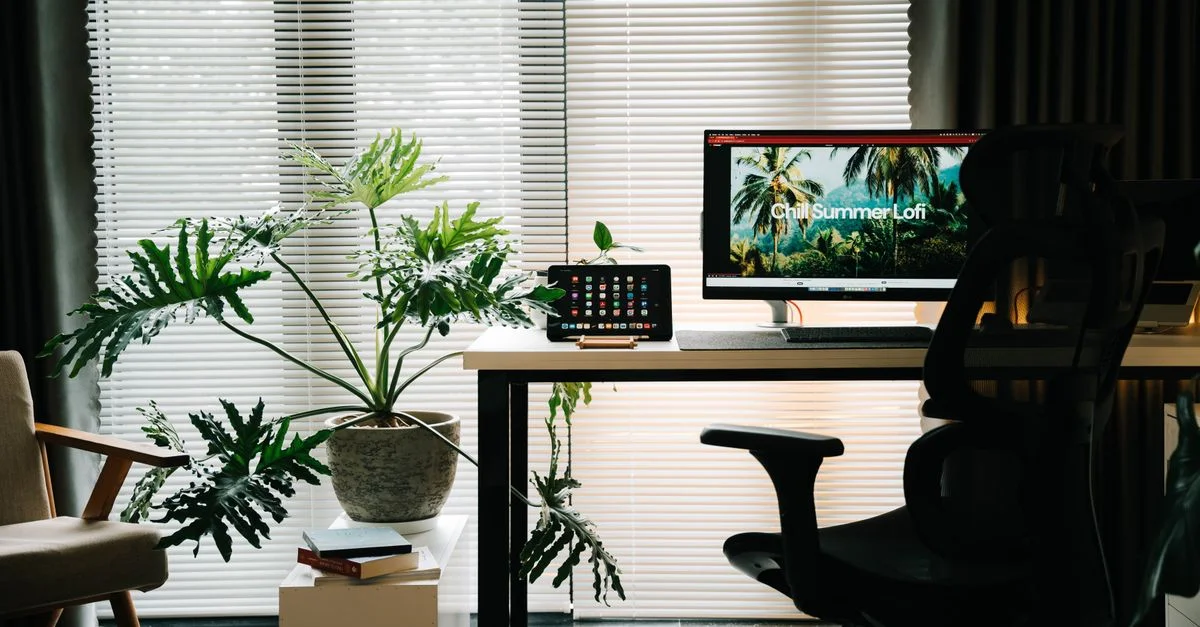 Bureau à domicile élégant avec grande plante, configuration informatique et esthétique minimaliste.