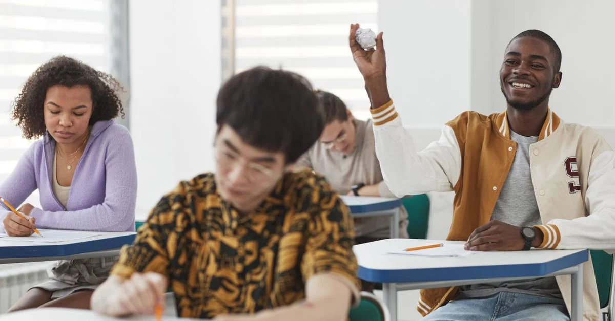 Des étudiants passant un examen dans une classe diversifiée, montrant un mélange de concentration et d'interactions ludiques.