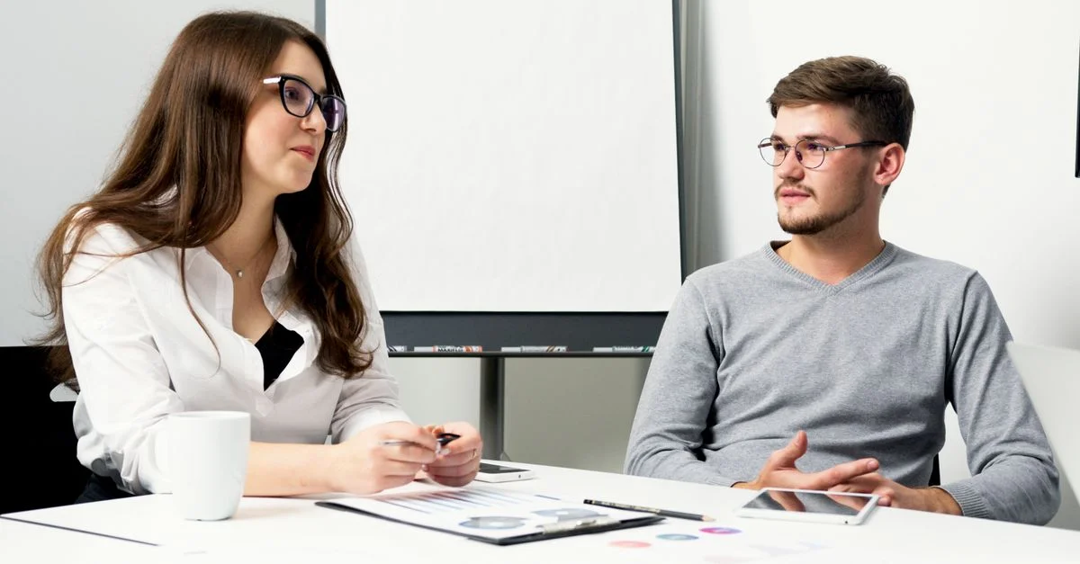 Deux professionnels dans un environnement de bureau discutant de leur travail autour d'un bureau avec des documents.