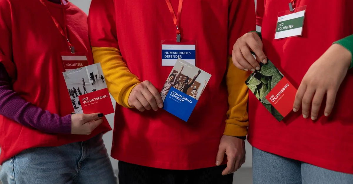 Des bénévoles en chemises rouges tenant des brochures informatives sur l'art et le bénévolat écologique.