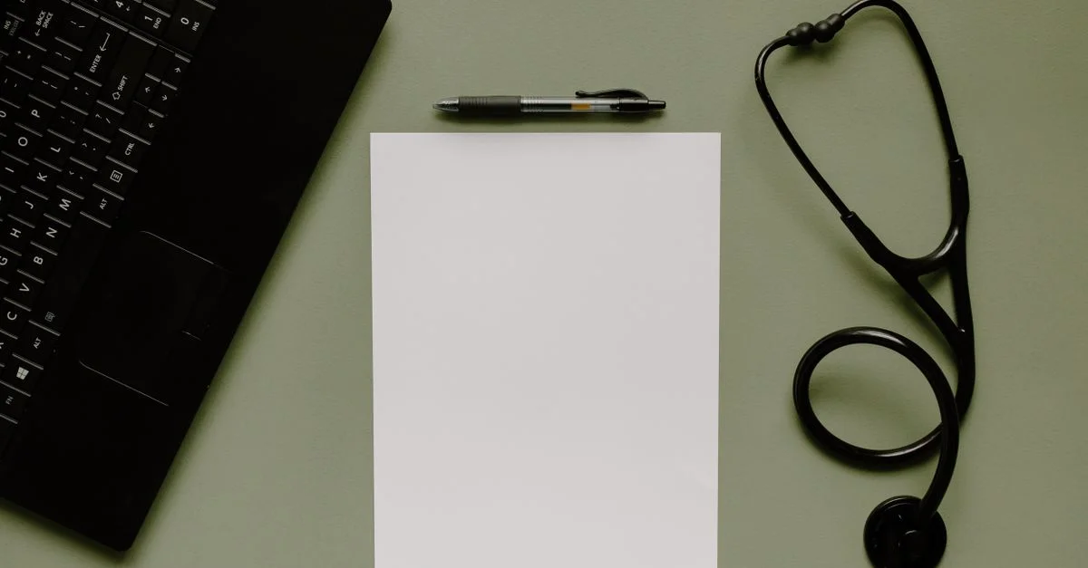 Espace de travail médical avec une feuille blanche, un stéthoscope et un ordinateur portable vus d'en haut.