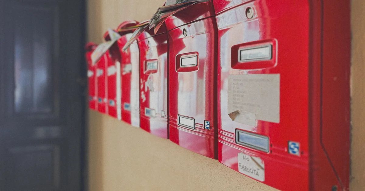 Rangée de boîtes aux lettres rouges débordant de courrier, symbolisant la communication et la correspondance à l'intérieur des bâtiments.