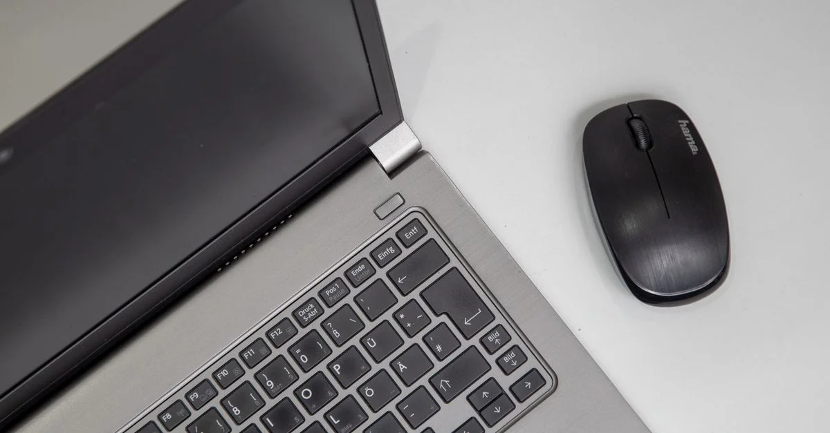 Vue de dessus d'un ordinateur portable avec une souris sans fil sur une table blanche.