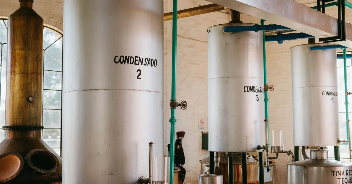 Vue intérieure d'une distillerie de tequila industrielle avec des cuves en métal et des tuyaux.