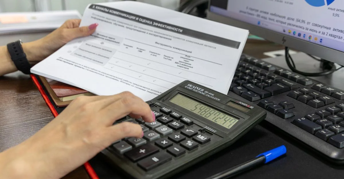 Une personne calcule des données financières à l'aide d'une calculatrice et d'un document, travaillant à un bureau.