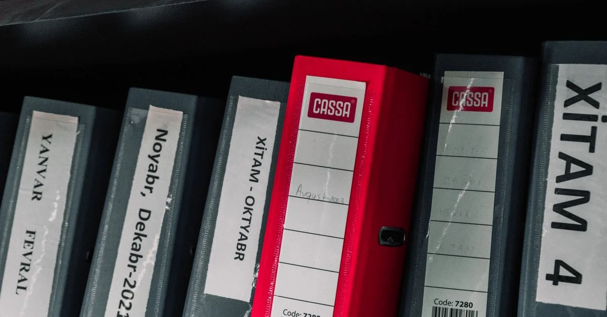 Classeur de bureau codés par couleur organisés soigneusement dans une étagère de rangement, avec des étiquettes et un classeur rouge frappant.
