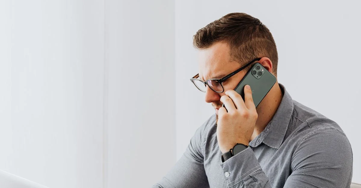 Homme professionnel avec des lunettes en communication téléphonique tout en travaillant sur un ordinateur portable.