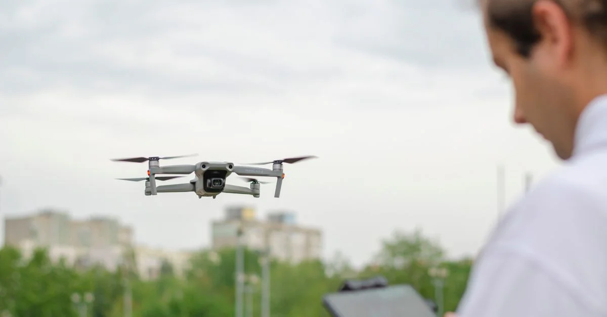 Drone en vol piloté par une personne dans un parc urbain, capturant un paysage urbain.
